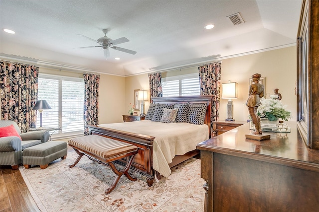 bedroom with light wood-type flooring, a textured ceiling, a raised ceiling, ornamental molding, and ceiling fan