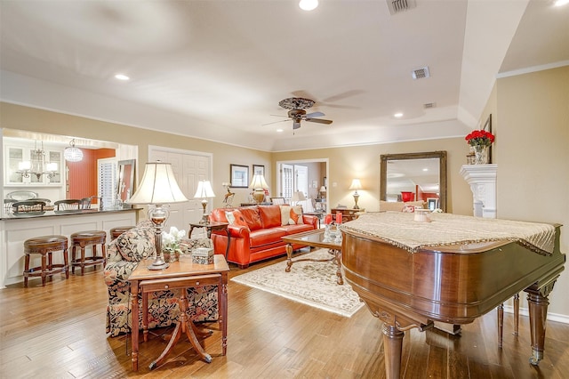 living room with ceiling fan with notable chandelier, wood-type flooring, and ornamental molding