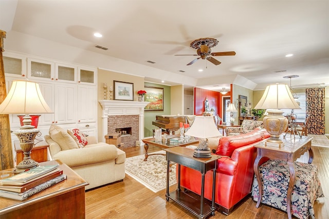 living room featuring ceiling fan, a stone fireplace, and light wood-type flooring