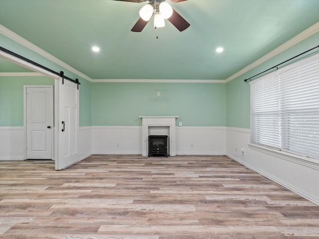 unfurnished living room featuring ceiling fan, ornamental molding, light hardwood / wood-style floors, and a barn door