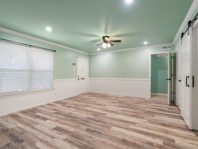 empty room featuring ceiling fan, ornamental molding, light hardwood / wood-style flooring, and a barn door