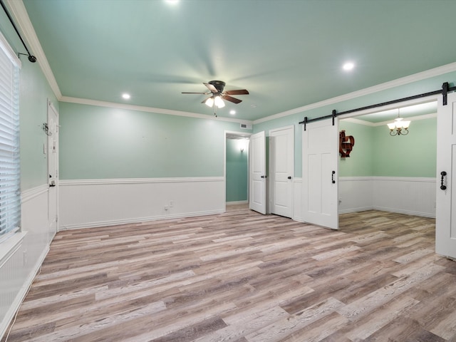 spare room with a barn door, ceiling fan with notable chandelier, light hardwood / wood-style floors, and ornamental molding