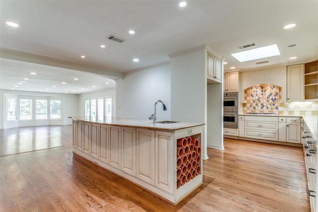 kitchen featuring a skylight, light hardwood / wood-style flooring, a kitchen island with sink, appliances with stainless steel finishes, and light stone countertops