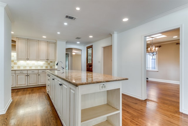 kitchen with backsplash, a kitchen island with sink, light wood-type flooring, and light stone countertops