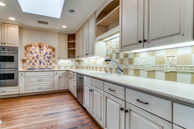 kitchen with light wood-type flooring, sink, decorative backsplash, a skylight, and appliances with stainless steel finishes