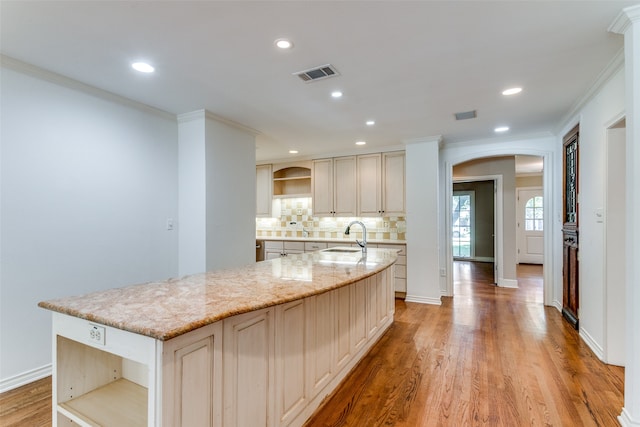 kitchen featuring decorative backsplash, light hardwood / wood-style floors, light stone counters, a kitchen island with sink, and sink