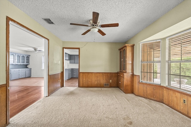 carpeted spare room with a textured ceiling, wooden walls, and ceiling fan