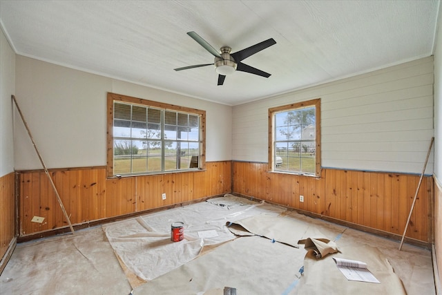 empty room with ceiling fan, wooden walls, and ornamental molding