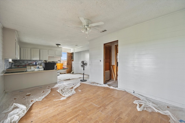 living room with a textured ceiling, wooden walls, ceiling fan, and light hardwood / wood-style flooring