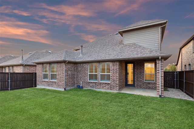 back house at dusk featuring a patio area and a yard