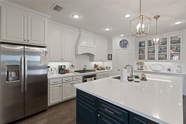 kitchen with sink, white cabinetry, custom range hood, stainless steel appliances, and a kitchen island with sink