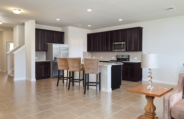 kitchen with dark brown cabinetry, a kitchen island, backsplash, stainless steel appliances, and light stone countertops