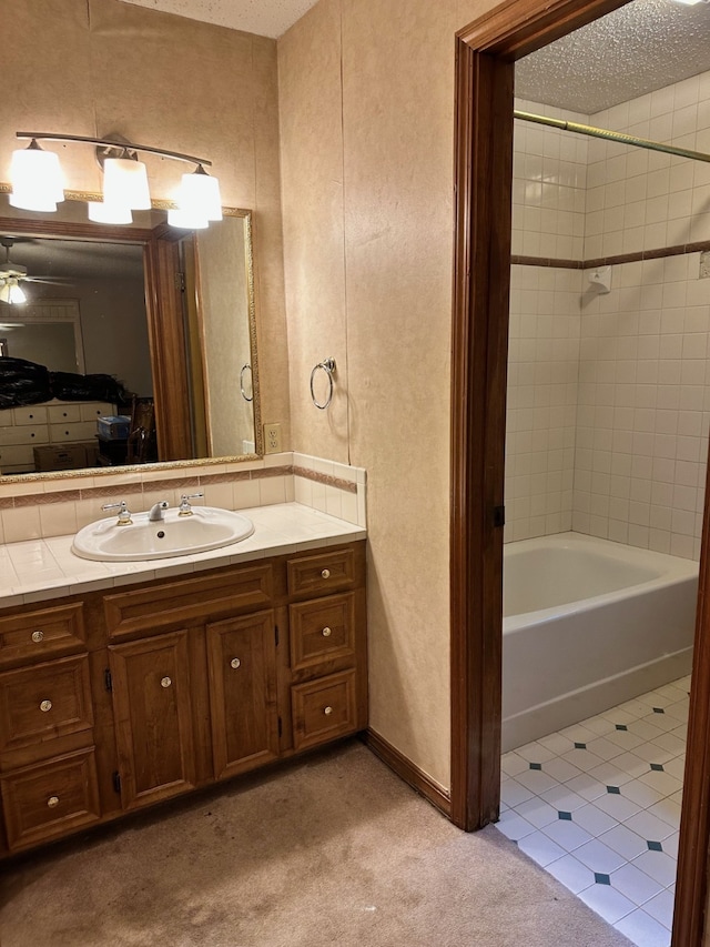 bathroom featuring ceiling fan, a textured ceiling, tiled shower / bath combo, and vanity