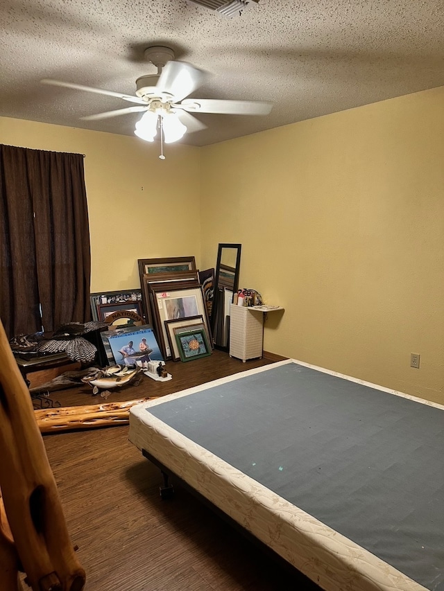 bedroom with a textured ceiling, dark wood-type flooring, and ceiling fan