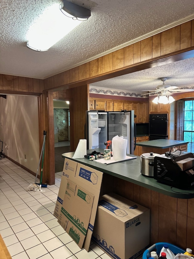 kitchen with ceiling fan, stainless steel fridge, wood walls, a textured ceiling, and black oven