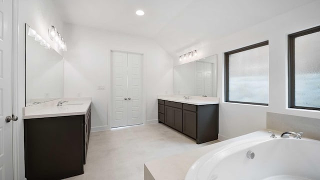 bathroom featuring a tub, lofted ceiling, two vanities, and a sink