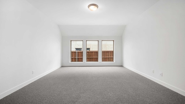 carpeted spare room featuring lofted ceiling and baseboards