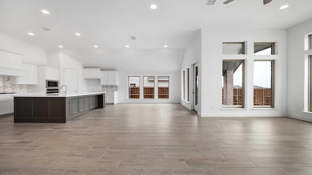 kitchen featuring stainless steel microwave, backsplash, open floor plan, white cabinets, and a sink