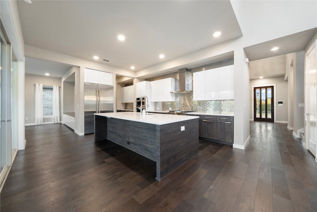 kitchen featuring wall chimney range hood, dark hardwood / wood-style flooring, high quality fridge, a center island with sink, and white cabinets