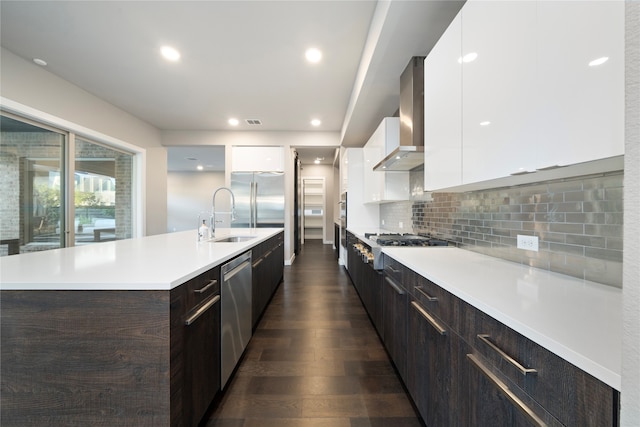 kitchen with dark wood-type flooring, white cabinets, wall chimney range hood, sink, and tasteful backsplash