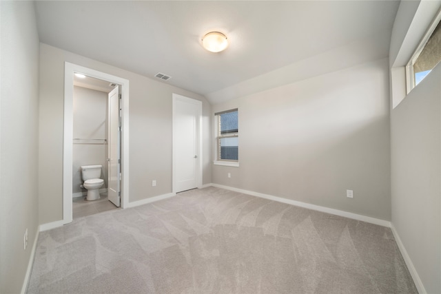 unfurnished bedroom featuring lofted ceiling, ensuite bathroom, and light colored carpet