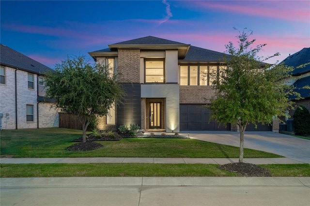 view of front facade featuring brick siding, stucco siding, a lawn, an attached garage, and driveway