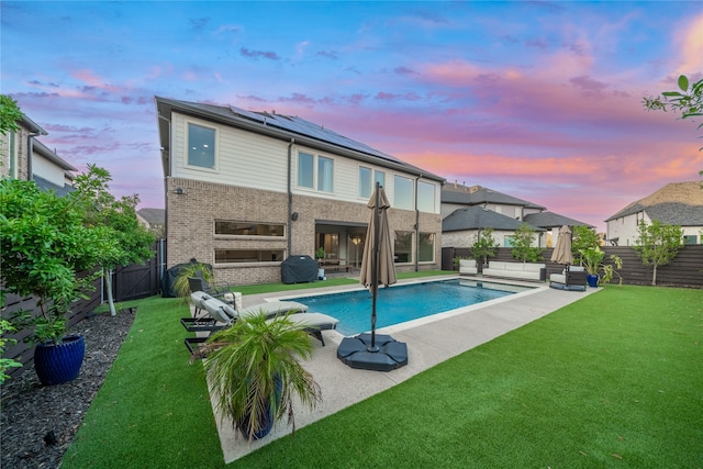 back house at dusk with solar panels, an outdoor living space, a patio, a fenced in pool, and a lawn