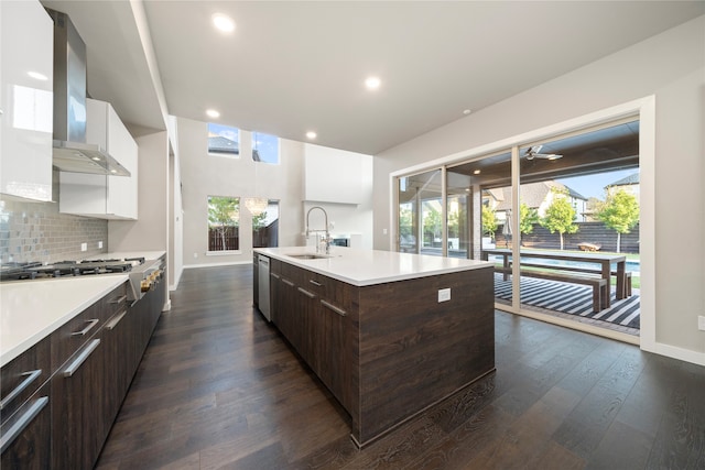 kitchen featuring an island with sink, white cabinetry, wall chimney exhaust hood, and sink