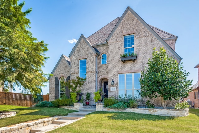 view of front of home with a front yard, brick siding, fence, and roof with shingles