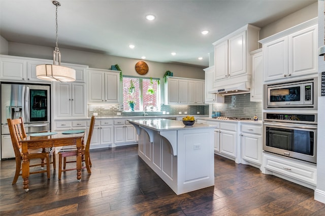 kitchen with white cabinets, stainless steel appliances, decorative light fixtures, and a center island