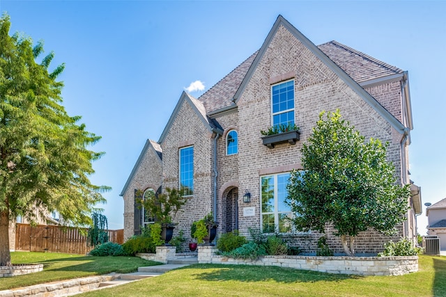 french country inspired facade with central AC unit, a front lawn, and brick siding