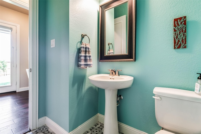 half bathroom featuring wood finished floors, toilet, and baseboards