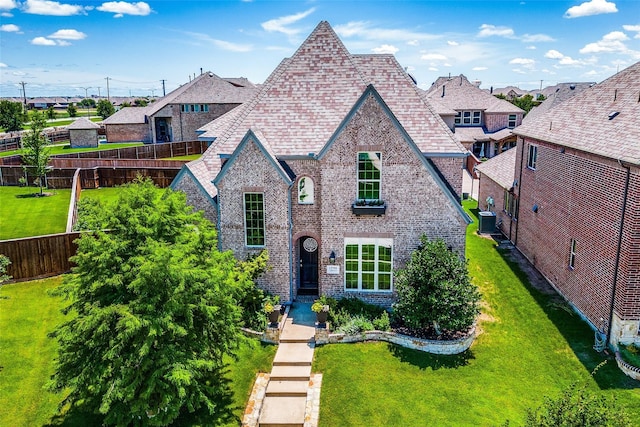 tudor house with a fenced backyard, central AC, brick siding, a shingled roof, and a front lawn