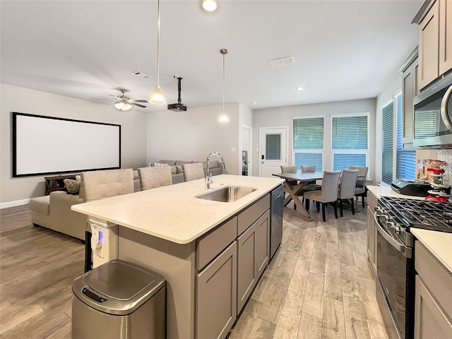 kitchen featuring ceiling fan, hanging light fixtures, sink, stainless steel appliances, and light hardwood / wood-style floors