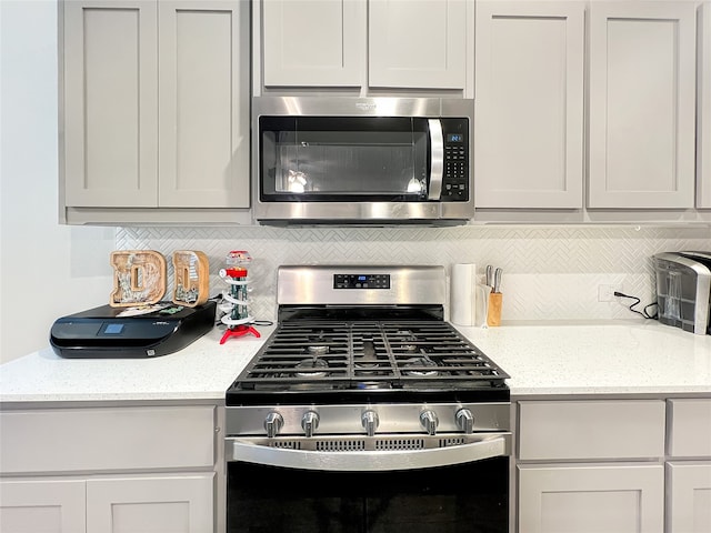 kitchen featuring light stone counters, white cabinets, stainless steel appliances, and backsplash