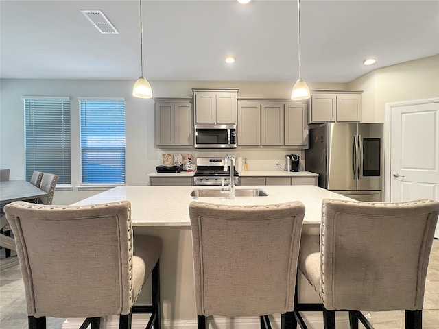 kitchen with gray cabinets, sink, an island with sink, hanging light fixtures, and stainless steel appliances