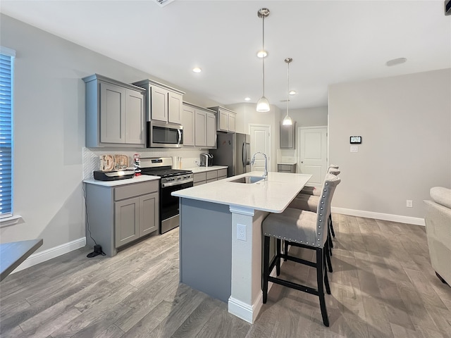 kitchen with appliances with stainless steel finishes, gray cabinetry, light hardwood / wood-style flooring, decorative light fixtures, and sink