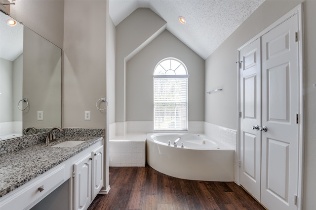 bathroom featuring vanity, lofted ceiling, a relaxing tiled tub, a textured ceiling, and hardwood / wood-style flooring