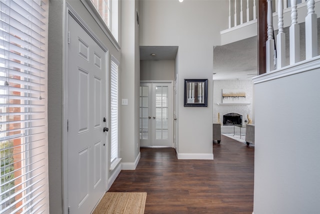 foyer entrance featuring a high ceiling, dark hardwood / wood-style flooring, a brick fireplace, and plenty of natural light