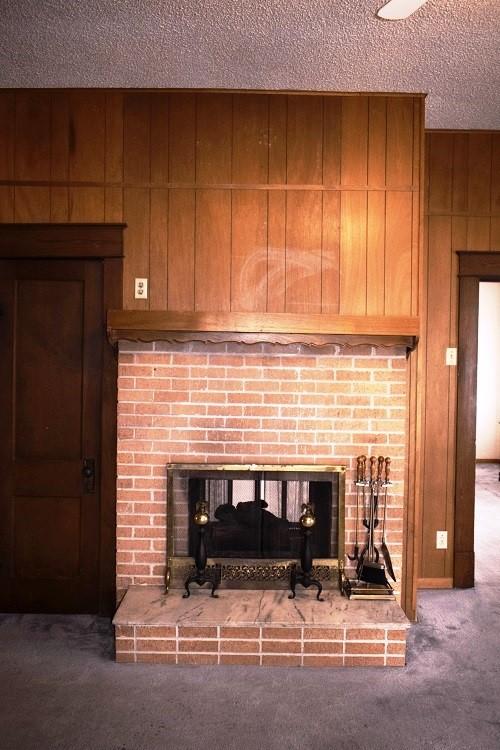 interior details featuring wooden walls, a brick fireplace, carpet flooring, and a textured ceiling