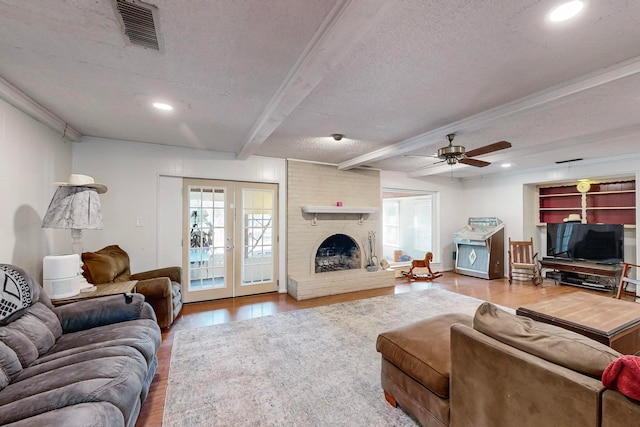 living room with a brick fireplace, beamed ceiling, a textured ceiling, ceiling fan, and hardwood / wood-style floors