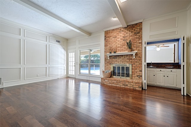 unfurnished living room featuring sink, a fireplace, a textured ceiling, beamed ceiling, and dark hardwood / wood-style floors