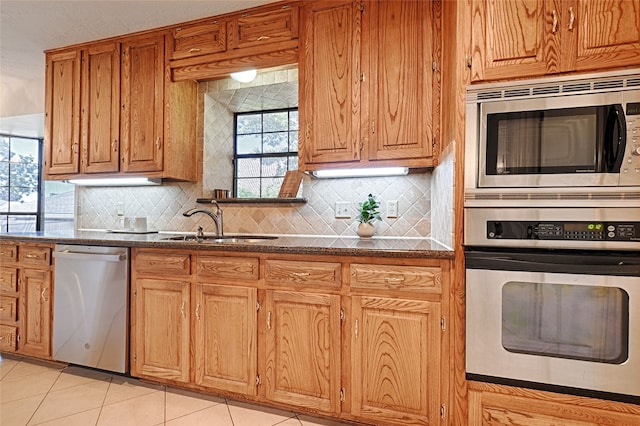 kitchen with light tile patterned floors, appliances with stainless steel finishes, backsplash, dark stone countertops, and sink