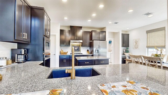 kitchen with dark brown cabinets, decorative backsplash, stainless steel appliances, light hardwood / wood-style flooring, and light stone countertops