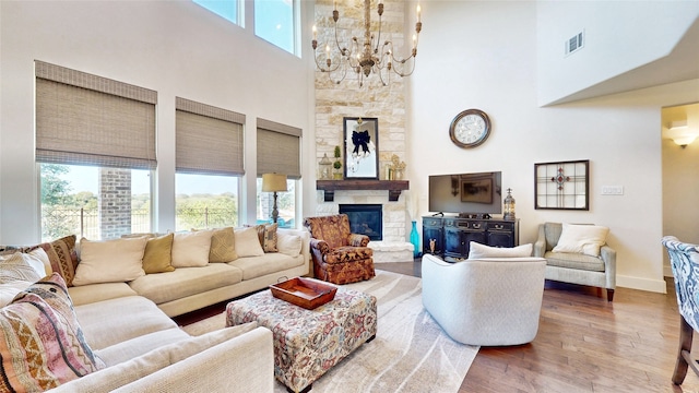 living room featuring wood-type flooring, a stone fireplace, a chandelier, and a healthy amount of sunlight