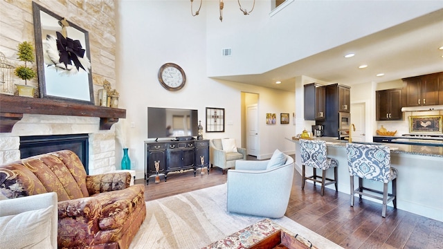 living room with a fireplace, a towering ceiling, and dark wood-type flooring