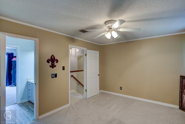 unfurnished bedroom with ceiling fan, a textured ceiling, light carpet, crown molding, and ensuite bathroom