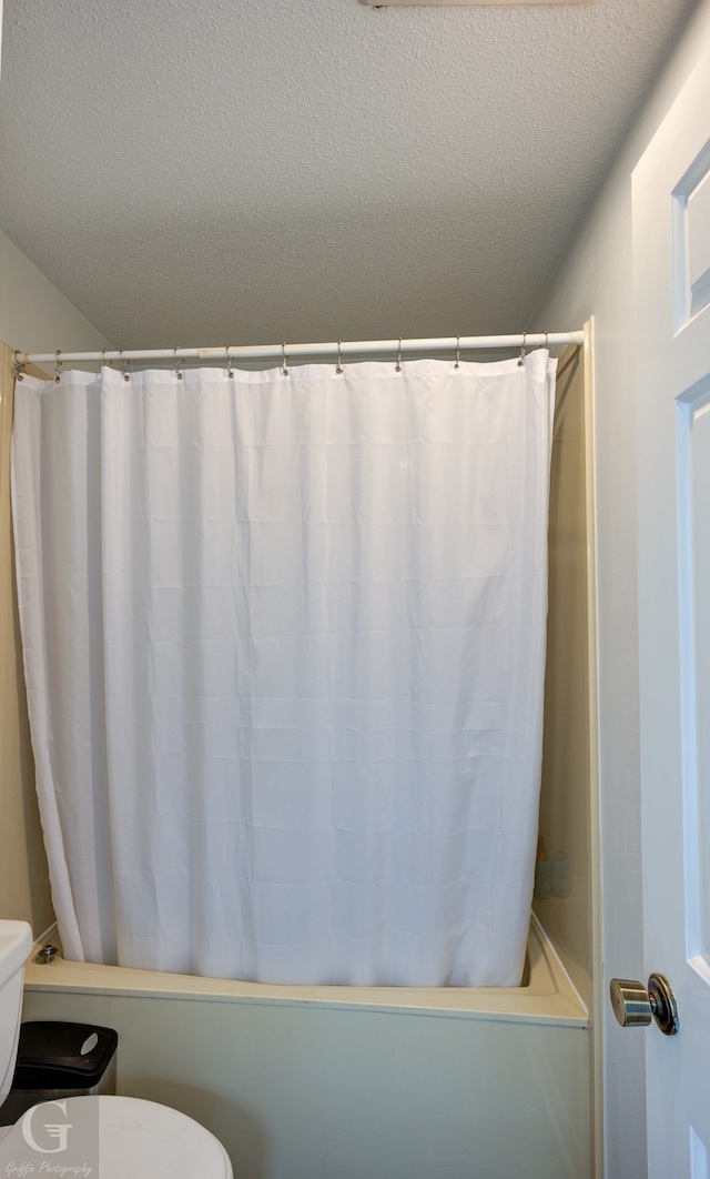 bathroom featuring shower / bath combination with curtain, a textured ceiling, and toilet