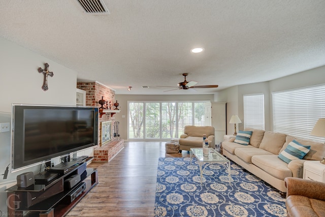 living room featuring a textured ceiling, wood-type flooring, a fireplace, and ceiling fan