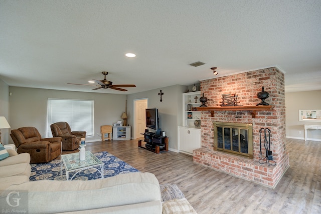 living room featuring ceiling fan, hardwood / wood-style flooring, a fireplace, and a textured ceiling